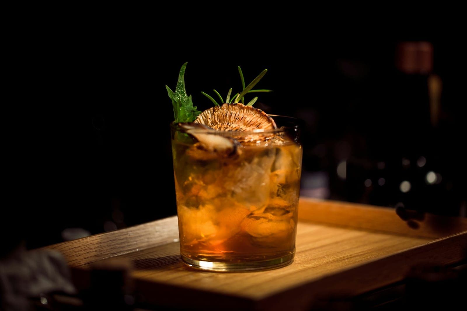 Craft cocktail with rosemary garnish in moody lighting